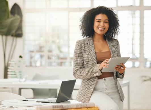 Smiling woman leaning on desk in office holding iPad